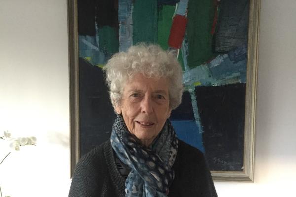 Carol Bolton, wearing a dark jacket and blue patterned scarf, stands in front of an abstract painting of green, red and blue