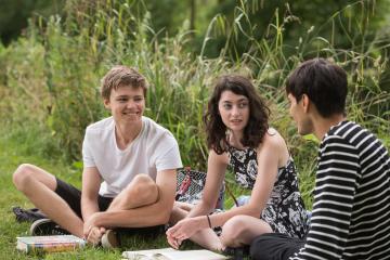 Three students talking outside sat on a grass lawn