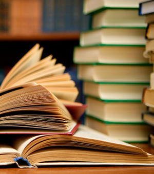 Pile of open books on table in front of book case